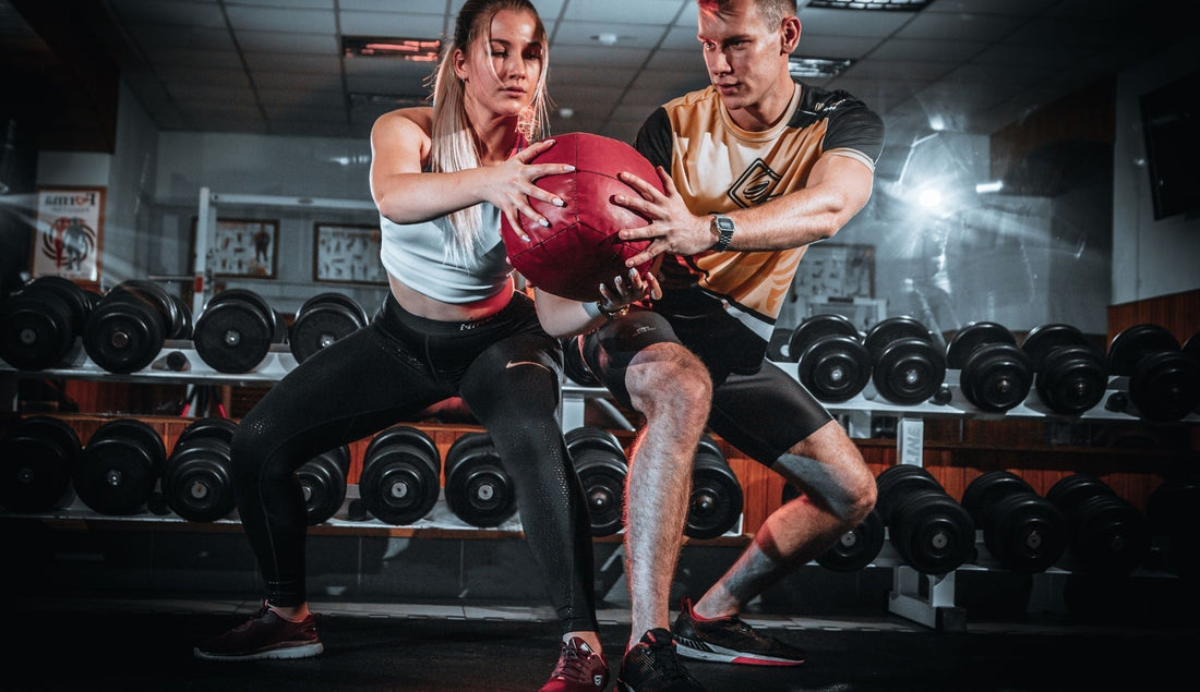 Two women training with a football in the gym to build strength and lean muscle using Anabolic Lean Mass supplement.